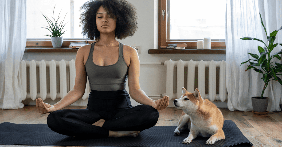 A woman sitting in the lotus position with her dog.